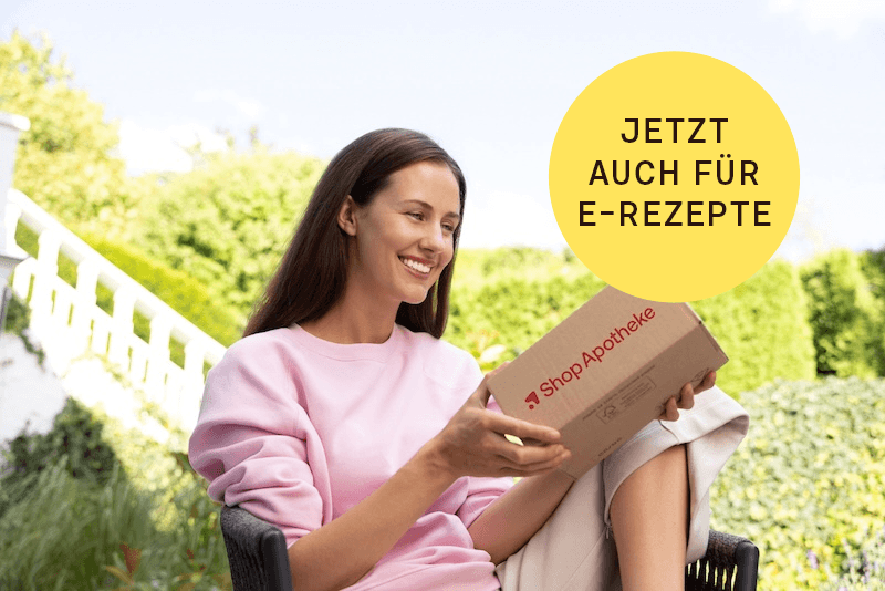 Eine lächelnde Frau sitzt im Garten und hält ein Paket von Shop Apotheke in der Hand.