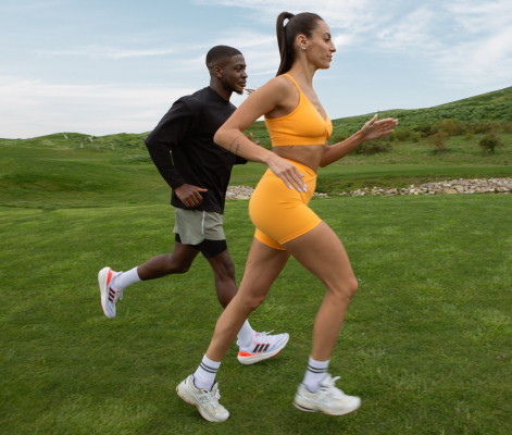 Una donna e un uomo in abbigliamento sportivo fanno jogging insieme su un prato verde sotto un cielo sereno.