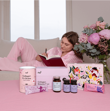 Frau liegt auf einer Couch und schreibt in ein Buch. Auf einem Tisch vor ihr stehen diverse nu3 Produkte.