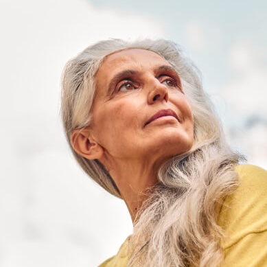 Femme aux cheveux gris courts rit de bon cœur au soleil.