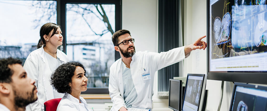 Gruppe von Ärzte schauen auf einen Bildschirm mit Gesundheitsdaten.