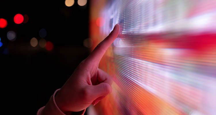 Nahaufnahme einer Hand, die einen großen leuchtenden Bildschirm mit bunten Farben berührt.