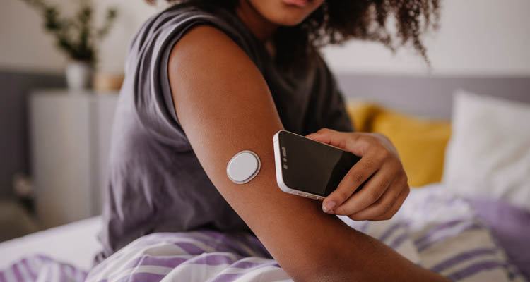 Eine Person hält ein Smartphone an einen Blutzuckersensor, der am Oberarm befestigt ist.