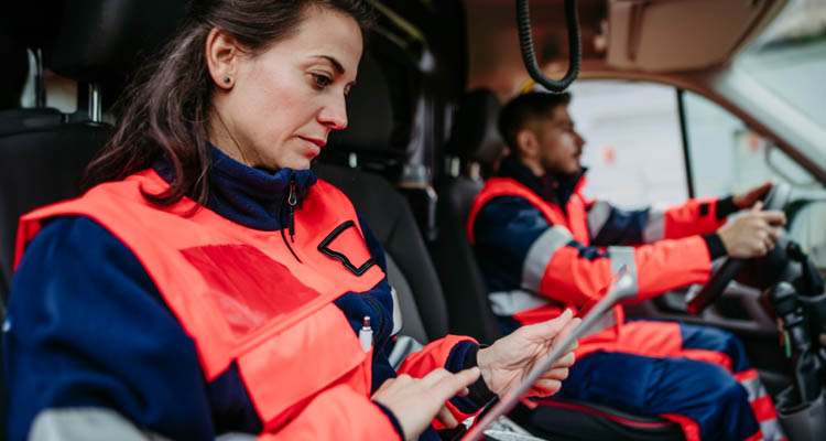 Eine Sanitäterin sitzt in einem Einsatzfahrzeug und arbeitet mit einem Tablet, neben ihr fährt ein Kollege.