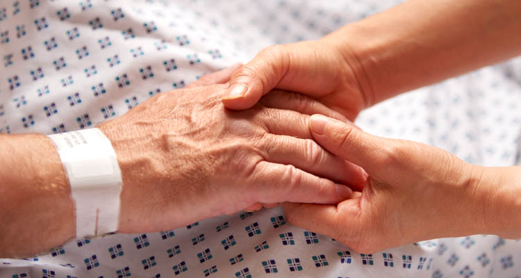 Älterer Mann sitzt auf Sofa und hält ein Smartphone in der rechten Hand.