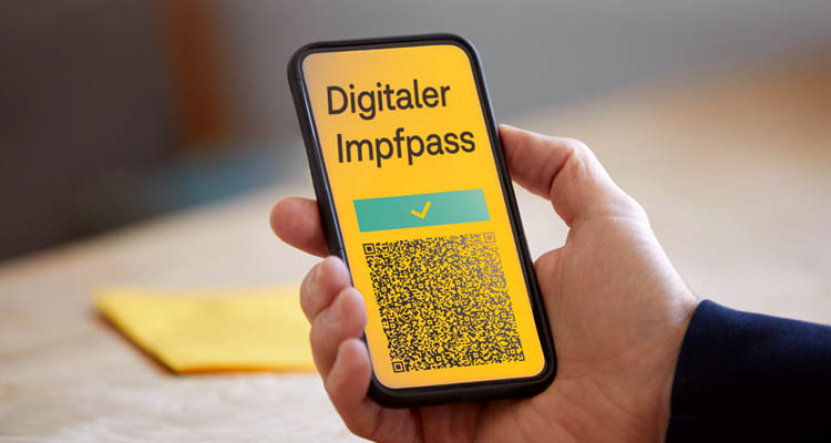 Eine Hand hält ein Smartphone, auf dem ein gelber Bildschirm mit der Aufschrift „Digitaler Impfpass“ und QR-Code angezeigt wird.