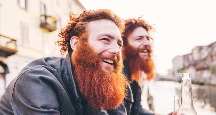 Zwei lachende Männer mit roten Vollbärten sitzen im Freien.