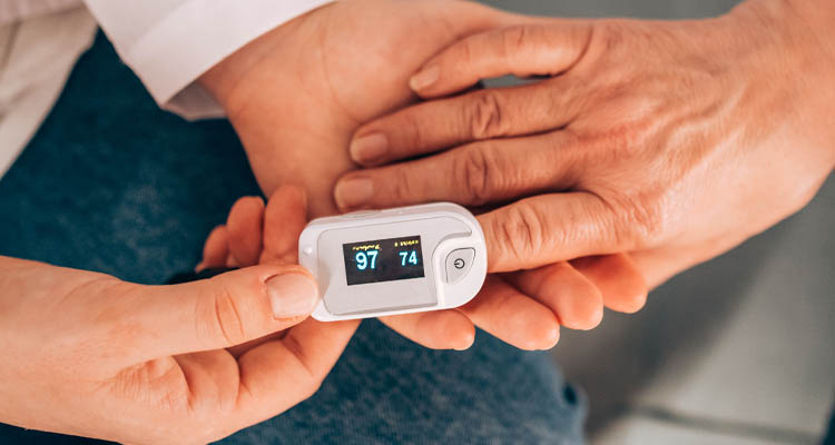Hand eines Arztes hält Pulsoximeter an Finger eines älteren Patienten, zeigt Sauerstoffsättigung und Puls an.