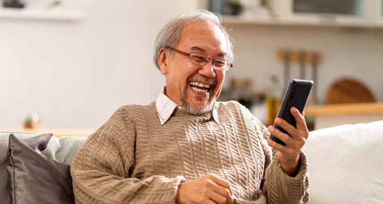 Älterer Mann sitzt auf Sofa und hält ein Smartphone in der rechten Hand.