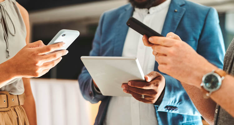 Drei Personen stehen zusammen, zwei halten Smartphones in der Hand, eine Person bedient ein Tablet.