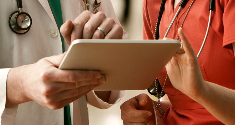 Zwei medizinische Fachkräfte, erkennbar an Stethoskopen, schauen gemeinsam auf ein Tablet.