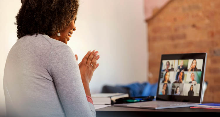Frau sitzt vor dem Laptop und hat eine Videokonferenz mit anderen Menschen.