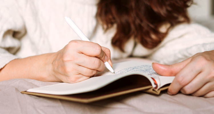 Nahaufnahme einer Person, die mit einem Stift in ein aufgeschlagenes Notizbuch schreibt.