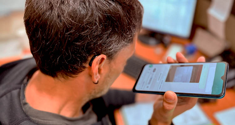 Mann mit Hörgerät hält Smartphone in der Hand und hört etwas ab.