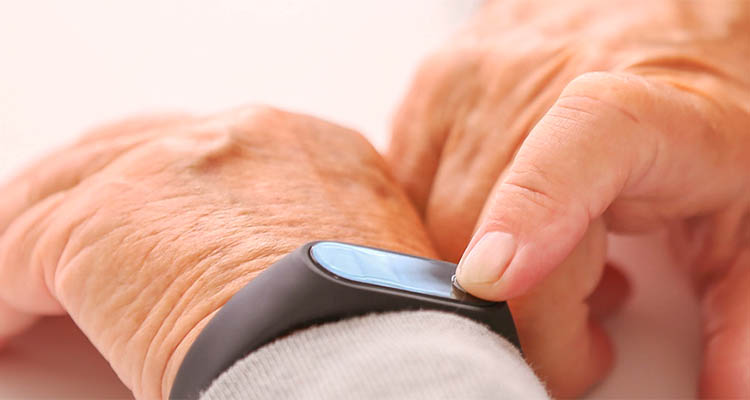 Nahaufnahme einer älteren Hand mit Smartband, auf das getippt wird.