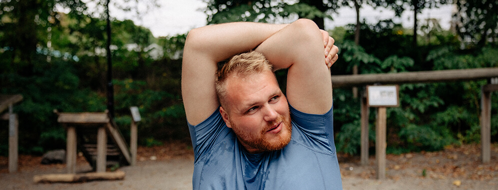 Junger kräftiger Mann macht Sport und dehnt sich den Oberkörper bzw. die Arme.