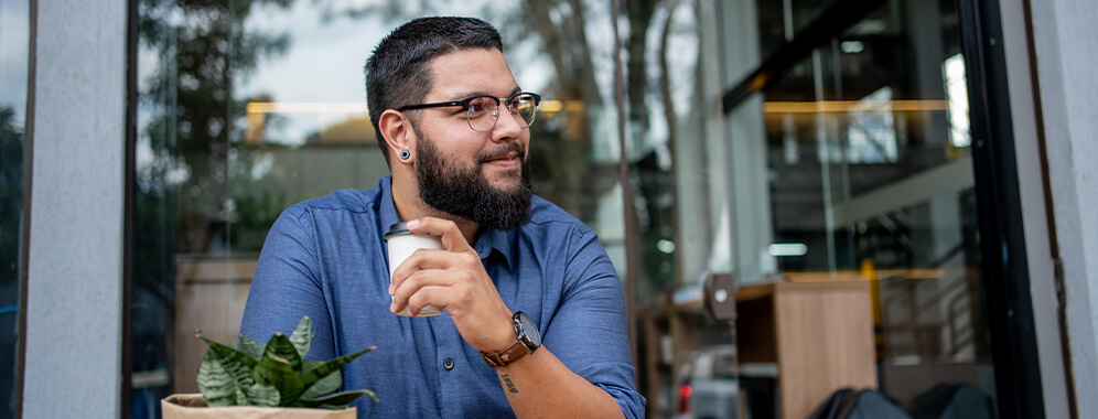 Junger Mann sitzt draußen in einem Café und trinkt aus einer Tasse.