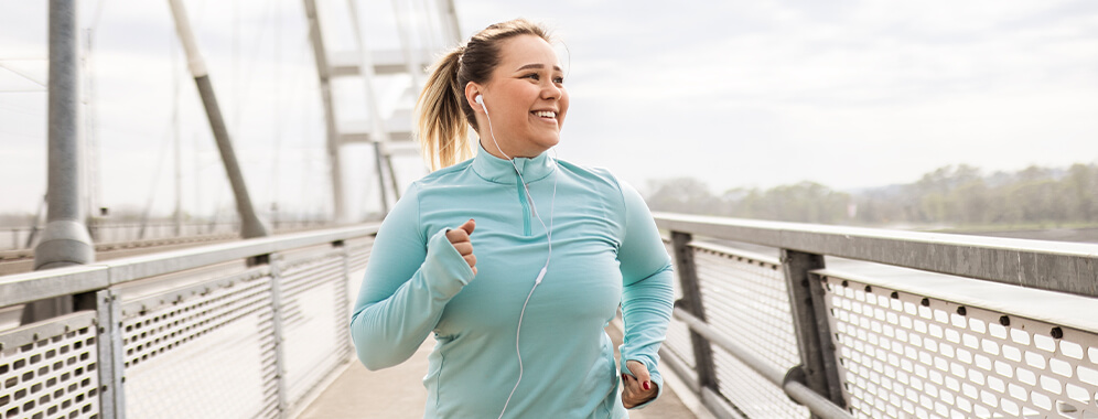 Eine junge, etwas kräftigere Frau lächelt beim Joggen.
