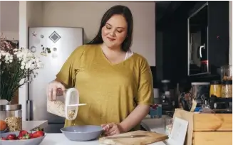 unge Frau in der Küche füllt Haferflocken in eine Schale und lächelt dabei.