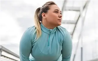 Junge Frau im blauen Sportoutfit macht Aufwärmübungen auf einer Brücke und blickt konzentriert zur Seite.