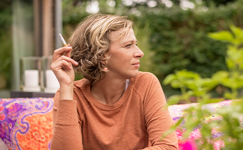 Eine Frau sitzt im Freien und raucht eine Zigarette.