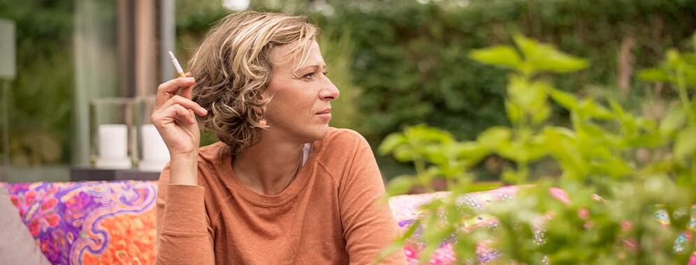 Eine Frau sitzt im Freien und raucht eine Zigarette.