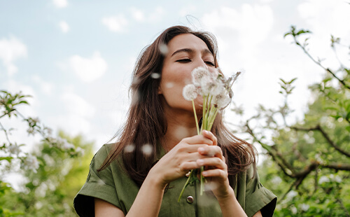 Eine Frau pustet in einen Strauß Pusteblumen. 