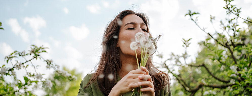 Eine Frau bläst in einen Strauß Pusteblumen.