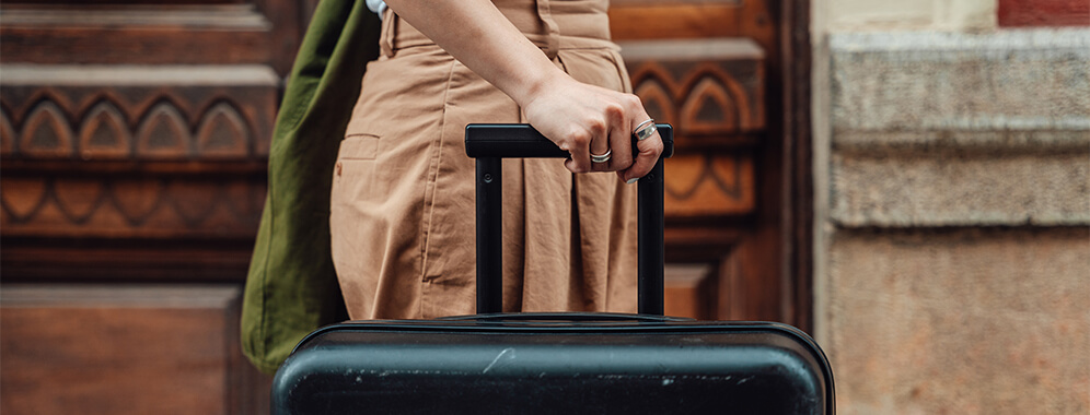 Ein Ausschnitt zeigt eine weibliche Person, die einen Koffer schiebt. 