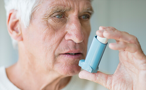 Ein älterer Herr hält einen Inhalator vor den Mund. 