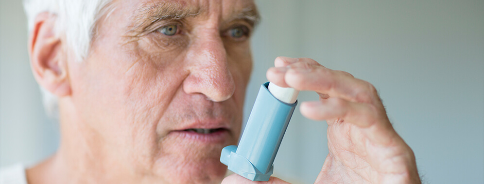 Ein älterer Herr hält einen Inhalator vor den Mund.
