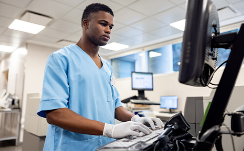 Eine Person steht in einem Labor am Computer und arbeitet.