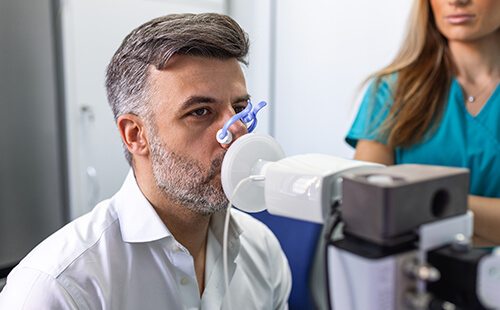 Ein Mann sitzt vor einem Gerät, seine Nase ist verschlossen. 