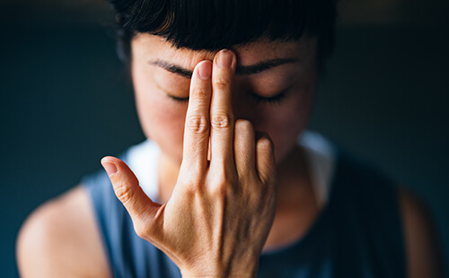 Eine Frau hält sich zwei Finger an die Stirn. 