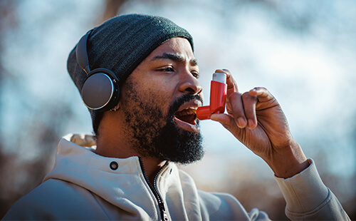 Ein Mann, der scheinbar draußen joggen war, benutzt einen Inhalator. 