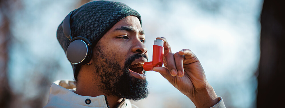 Ein Mann, der scheinbar draußen joggen war, benutzt einen Inhalator.