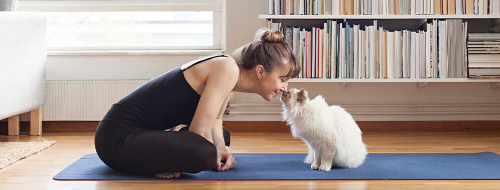 Eine Frau kuschelt mit ihrer Katze auf einer Yogamatte.