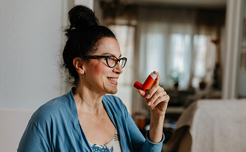 Eine Frau hält einen Inhalator in der Hand. 