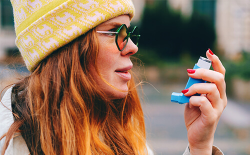 Eine Frau hält einen Inhalator vor den Mund. 
