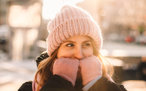 Eine Frau ist im Winter draußen, sie trägt Mütze und Handschuhe und lächelt.