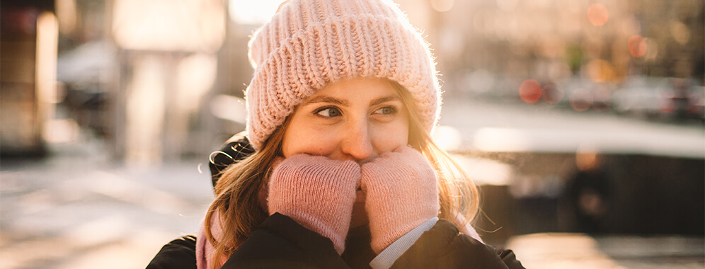 Eine Frau steht im Winter draußen, sie trägt Mütze und Handschuhe und lächelt.