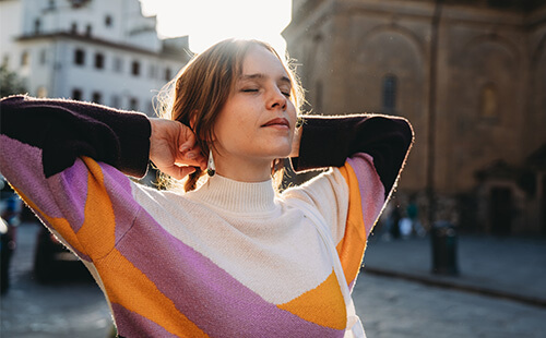 Eine Frau steht mit geschlossenen Augen in einer Stadt und atmet ein. 