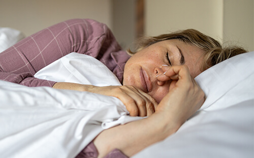 Eine Frau liegt mit geschlossenen Augen im Bett.