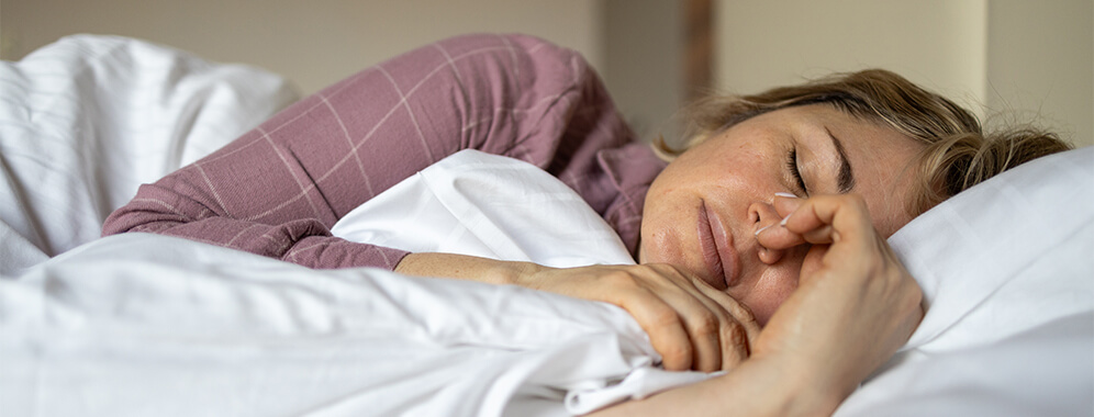 Eine Frau liegt mit geschlossenen Augen im Bett.
