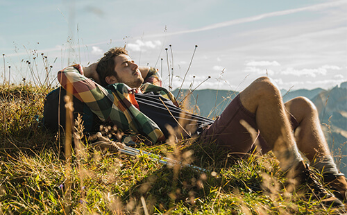 Ein Mann macht eine Wanderpause und liegt auf dem Rücken in den Bergen. 