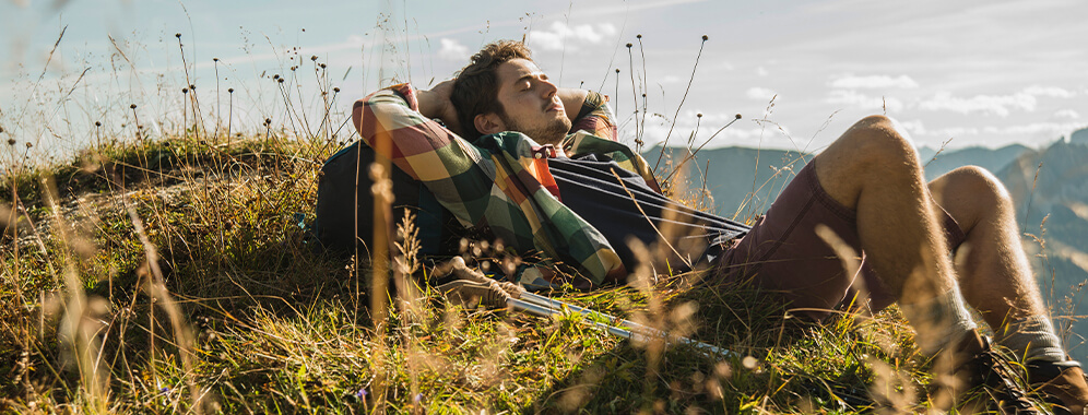 Ein Mann liegt mit geschlossenen Augen auf einem Berg und macht eine Wanderpause.