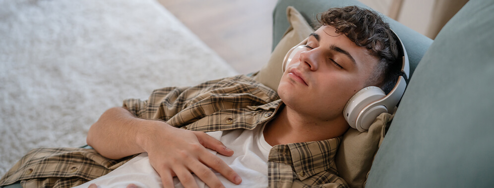 Ein junger Mann liegt mit Kopfhörern auf der Couch. 