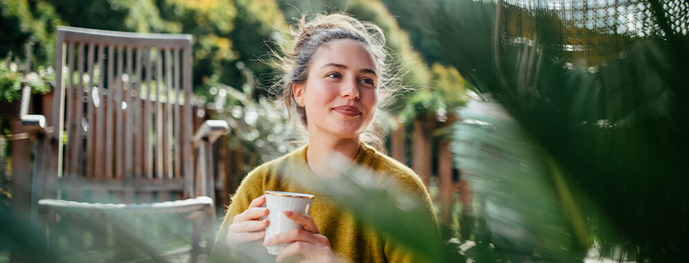 Eine Frau sitzt draußen und hält eine Tasse in der Hand. 