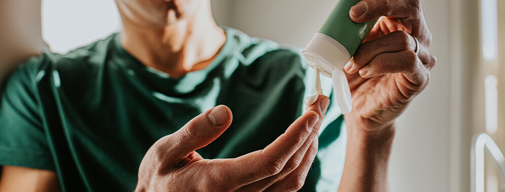 Ein Mann entnimmt Creme aus einer Tube. 