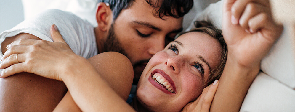 Ein Paar liegt Arm in Arm im Bett.